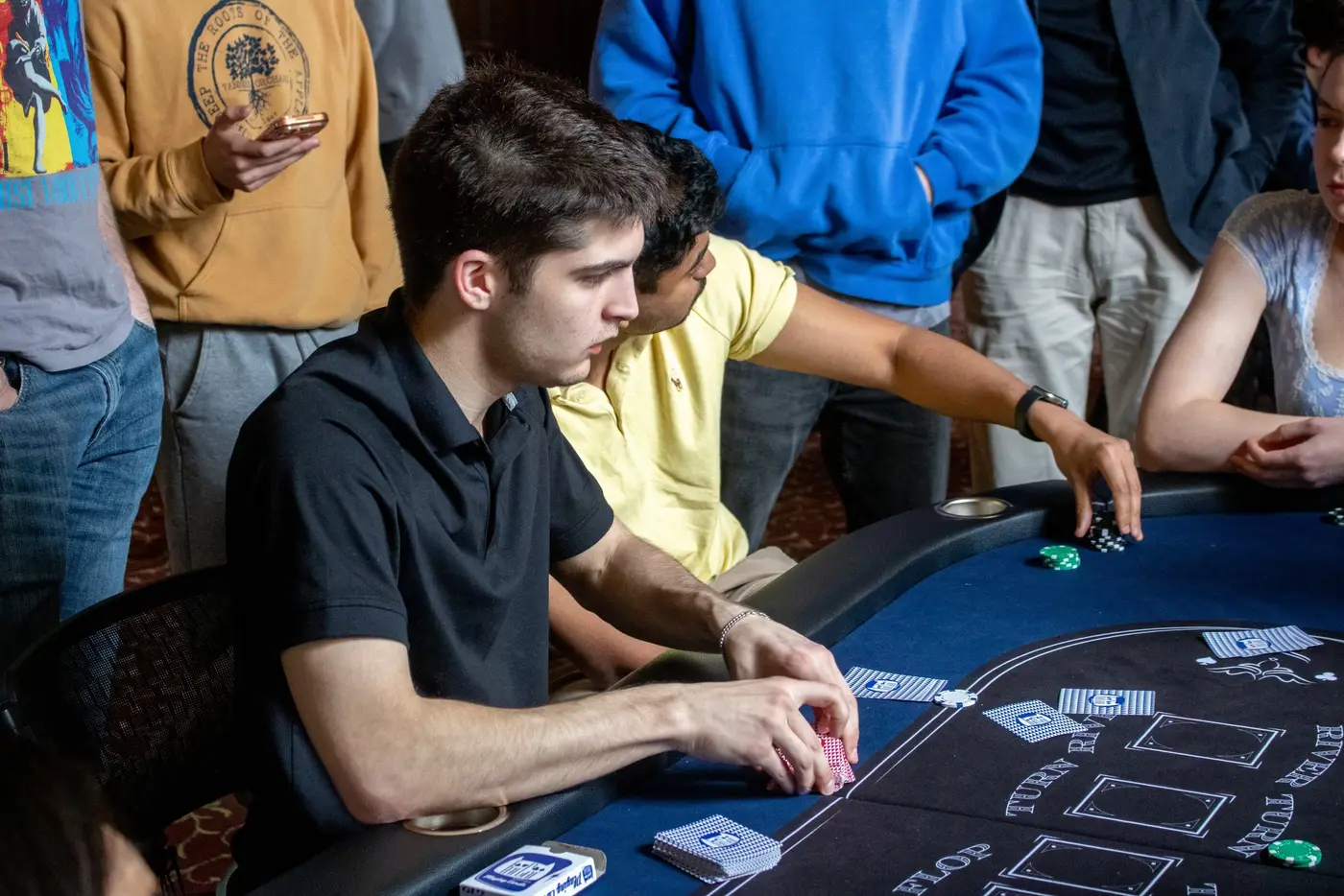 A crowd gathers around a table as a player checks his cards